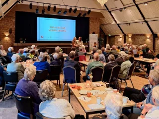 Een overzichtsfoto van een zaal vol mensen bij de bijeenkomst Dementie en Mantelzorg